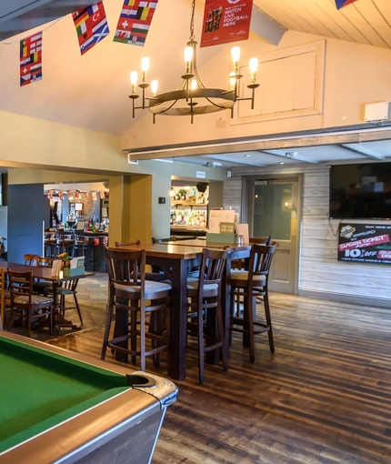 Interior dining area of a pub with a pool table, a bar and a TV.