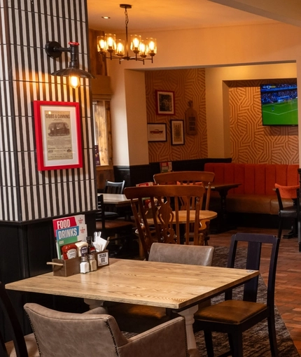 The bar and interior restaurant seating area at The Amington in Tamworth, with bottles of alcoholic spirits on a wooden shelf behind the counter, and TVs on the walls.