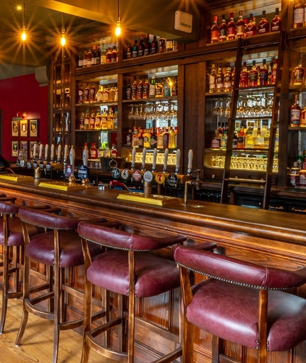 The wood panelled bar and interior restaurant seating area at The Beehive Inn, with upholstered chairs and bar stools, and a TV on the wall.