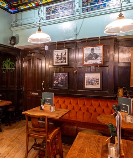 An interior restaurant seating area of The Two Brewers in Covent Garden, with dark wood panelled walls, a stained glass panel on the ceiling, a TV on the wall, and a fireplace.