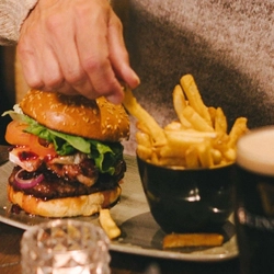 Two people sitting at a restaurant table, a burger served on a plate with a small bowl of fries and a plate of roast dinner sitting in front of them. A glass of Guinness and a Christmas cracker also sit on the table, and a Christmas tree is visible in the background.
