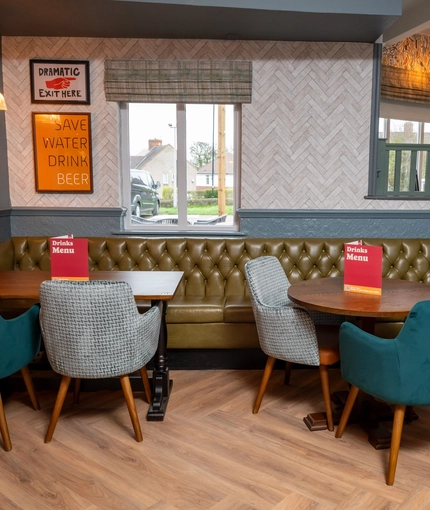 An interior restaurant seating area at the Devonshire Arms, with a large, upholstered corner seat, and framed artwork on the walls.