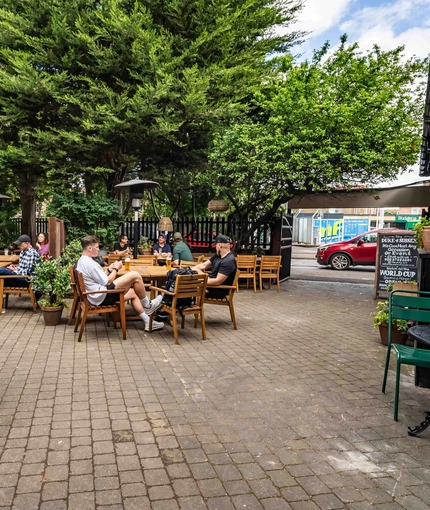 The exterior patio beer garden seating area with wooden tables, chairs, heaters and lighting at The Duke Of Sussex.