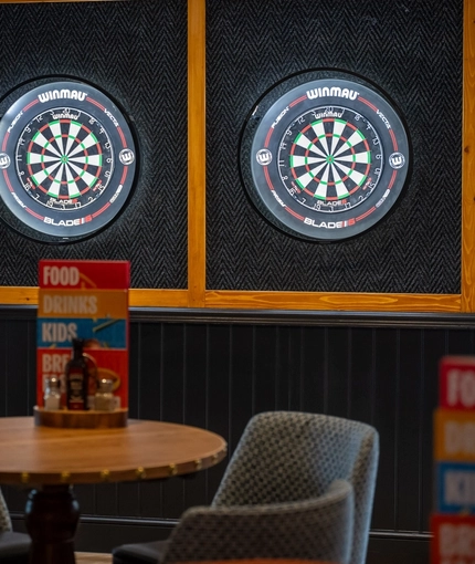 Two illuminated dartboards on the wall of one of the interior restaurant seating areas at The Heron.