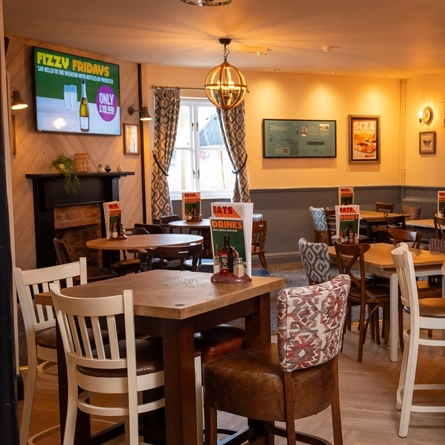 The interior restaurant seating area at The Woodlands Edge in Wiltshire; with a fireplace, and a TV on the wall above it.