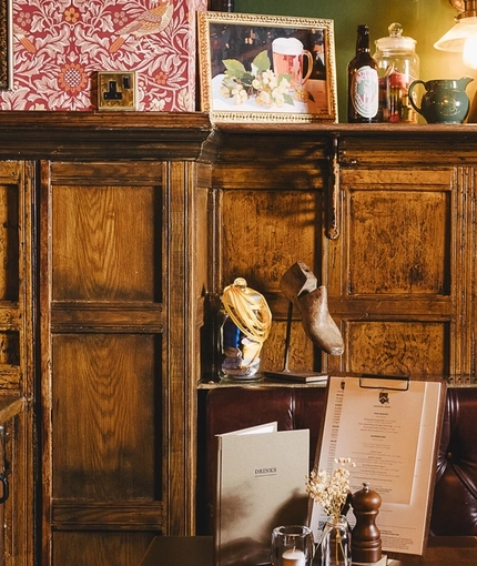 The wood panelled interior restaurant seating area at the Masons Arms, with upholstered booth seating, a fireplace, and grape vines carved into the coving.