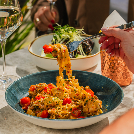 A lifestyle image showing a person enjoying a bowled pasta dish and glass of white wine at a Crafted venue.
