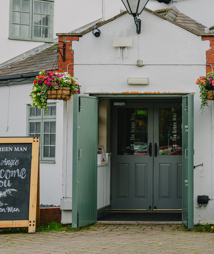 The exterior facade, signboard, and entrance to The Green Man in Brackley Hatch, with flower baskets hanging on the walls. 