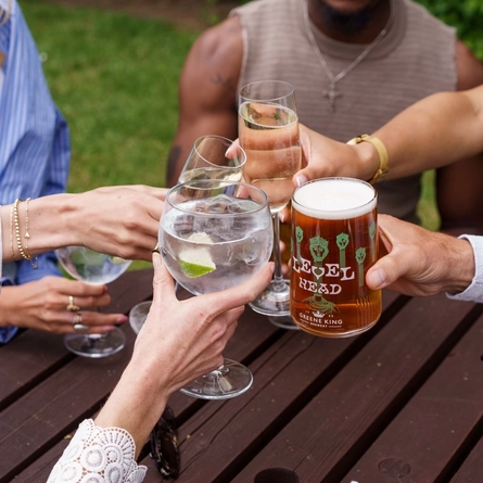 A close up image focusing on various drinks being held within an exterior beer garden seating area.