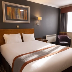 A hotel room at The Weathervane, with bed, chair, bedside tables, wall lights and wall art.