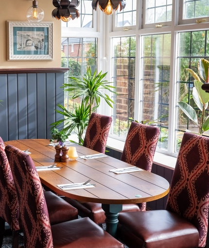 The interior restaurant seating area with tables, chairs, cushioned seating, potted plants and wall mounted TV at The Church View Inn.