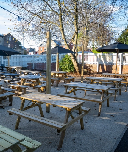 The exterior beer garden seating area at The Horsforth in Horsforth, with wooden picnic tables, shade umbrellas, and string lights overhead.