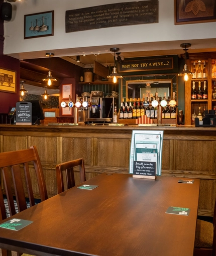 The bar and interior restaurant seating area at The Fox in Bury St Edmunds, with a wood panelled bar, and framed artwork on the walls.