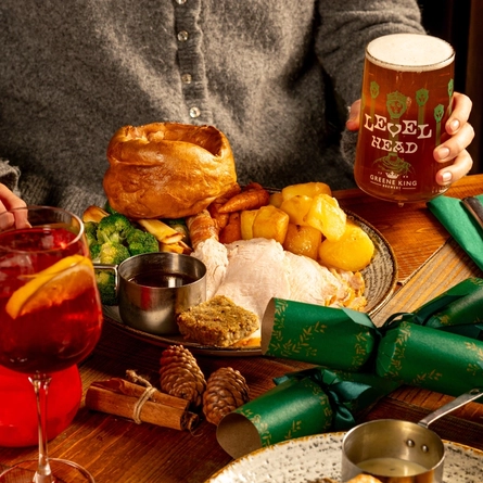 A person is seated at a wooden table, decorated with festive decoration.  There is a plated Christmas dinner in front of them.  Only the torso is visible in the image.