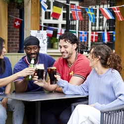 A mixed group of people sitting at an outdoor table, enjoying watching sport and drinks.