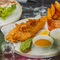 A plated fish, chips and peas dish with a Chicken Kyiv dish in the background sat on a table within the exterior beer garden seating area at a Crafted venue.