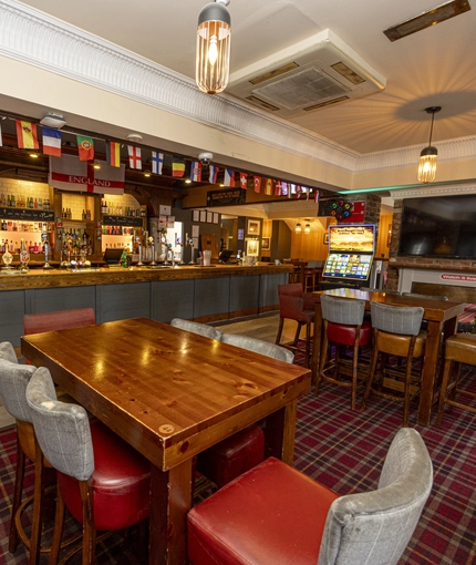 Interior dining area of a pub with a bar, a TV, a fireplace and a gambling machine.