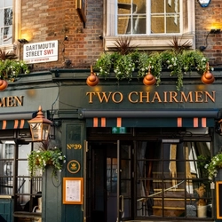 The exterior facade, signage, and seating area of the Two Chairmen in St James's, with flower baskets and large golden lanterns on the walls.