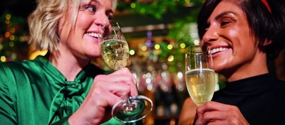 An image of 2 people enjoying sparkling white wine drinks within the interior seating area at a Greene King pubs venue.