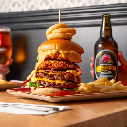 A close up image of a burger and various drinks sat on a table within the interior restaurant and seating area at a Hungry Horse venue.