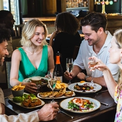 several main meals spread across table with people sitting around the table talking