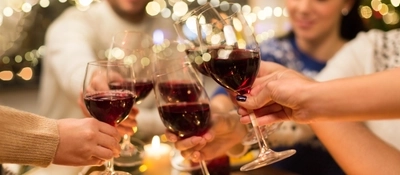 Some glasses of red wine being cheersed at a table.