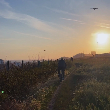 An image of a single track at sunset.  A person is cycling up the track, slightly uphill.