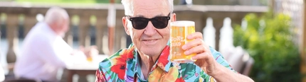 A image of Larry Lamb sat in a beer garden with a microphone and holding a pint of Level Head.