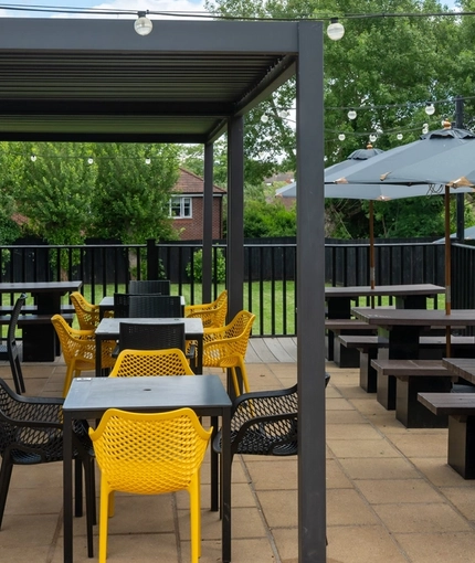 The paved exterior beer garden seating area of The Amington in Tamworth; with wooden picnic tables, shade umbrellas, string lights, and an under cover section.