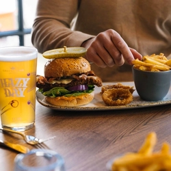 A close up image of a person sat at a table within the interior restaurant seating area enjoying a pint of Hazy Day and a Burger dish at a Heritage venue.