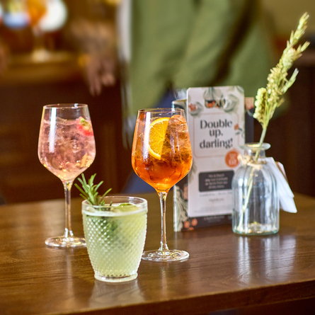 An advertising image of 3 cocktail style drinks sat on a wooden table within the interior seating area at a Chef & Brewer venue.