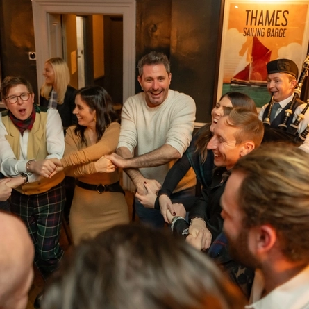 An image of a Bagpipe Player performing as people join hands to celebrate Auld Lang Syne within the interior function room during a Burns Night Event at The Crabtree.