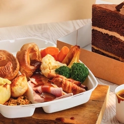 A takeaway box with a carvery inside it, next to a takeaway box with a slice of cake in it.