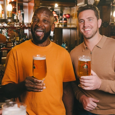 An image of 3 friends stood holding pints of Birra Moretti within the interior bar area at a Greene King venue.