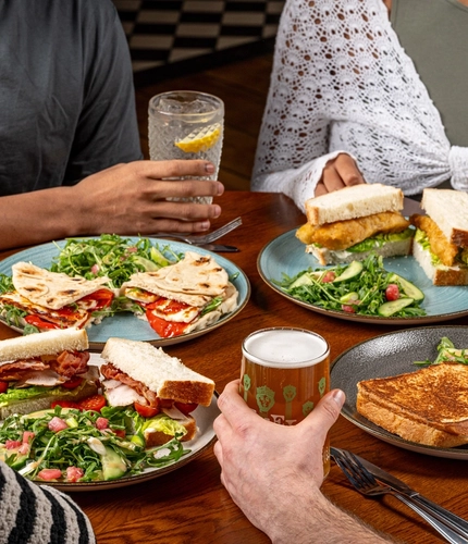 A table of food and drinks with some hands holding the drinks.