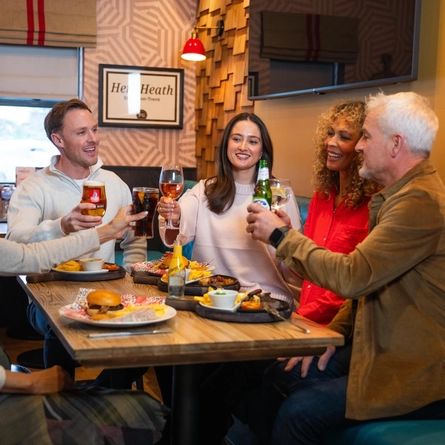 A mixed group seated at an indoor table holding drinks.  There are plates of food in front of them.