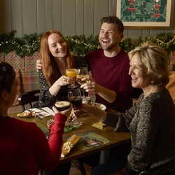 An image showing a group of people sat at a table within the interior restaurant seating area enjoying Festive drinks and celebrating with a cheers at a Chef & Brewer venue.