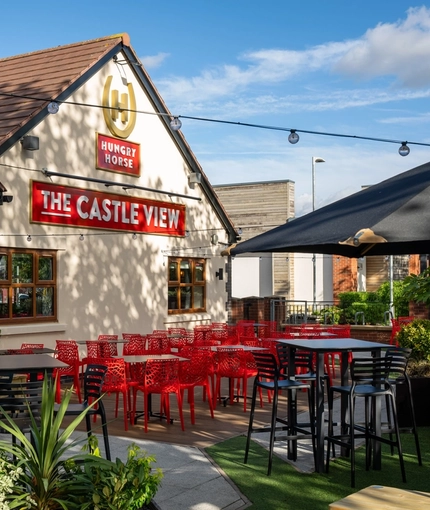 The exterior of the venue and beer garden seating area with tables, chairs, planters and string lighting at The Castle View.