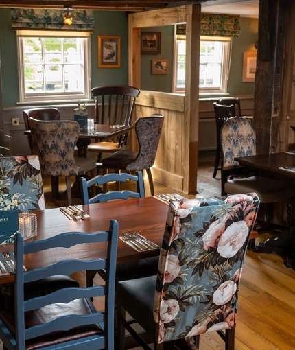 The interior restaurant seating area at The Kings Arms in Sandford-On-Thames, with wooden flooring and beams, upholstered chairs, and exposed brick wall details.