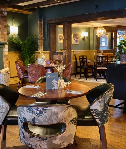 The interior restaurant seating area of the Smiths Arms pub, with fireplace, wooden beams, upholstered seats and wooden tables.