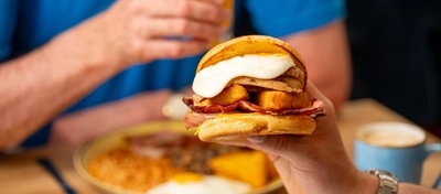 An image of 2 people, one enjoying a breakfast cob and a full English breakfast in the background within the interior of a Hungry Horse venue.