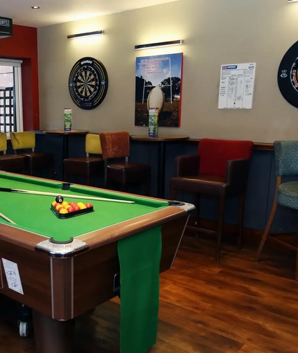 Interior dining area of a pub with a pool table, a TV and a few dartboards.