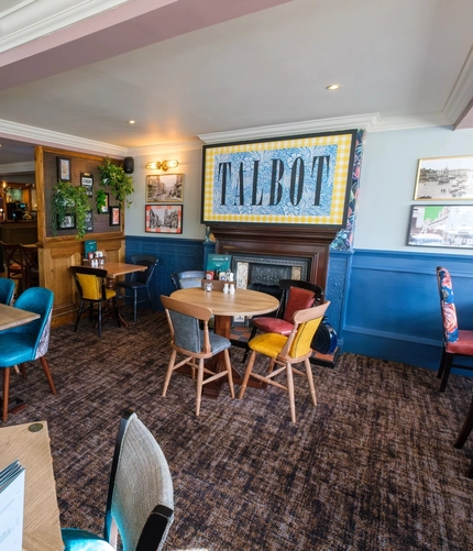 An interior restaurant seating area of The Talbot Inn, with framed artwork and potted plants on the walls, and a fireplace.
