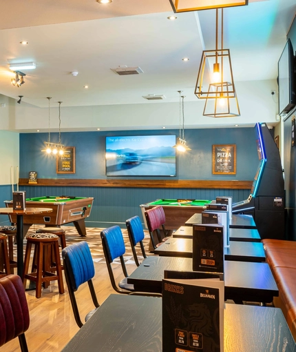 The interior seating area with the pub games area coming into view in the background including pool tables, a dart board, slot machine and TV at the Armstrongs. 