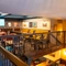 A view from the balcony of another upper floor restaurant seating area inside the Old School House, with a long, upholstered booth seat along one side of the room, framed artwork on the wall above it, and a TV on another wall.