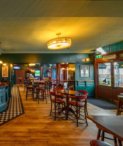 The ground floor bar and interior restaurant seating area at The Globe; with checkerboard tiles in front of the counter, TVs on the walls, two gaming machines, and bar stool seating.