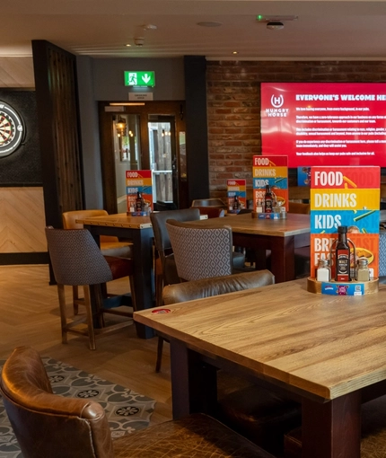 The interior restaurant seating area with tables, chairs, exposed brick wall with TV screen and dartboard in the background at The Castle View.