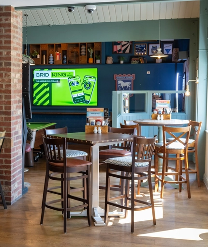 The interior restaurant seating area of The Man On The Moon, with TVs on the walls and wooden tables and chairs.