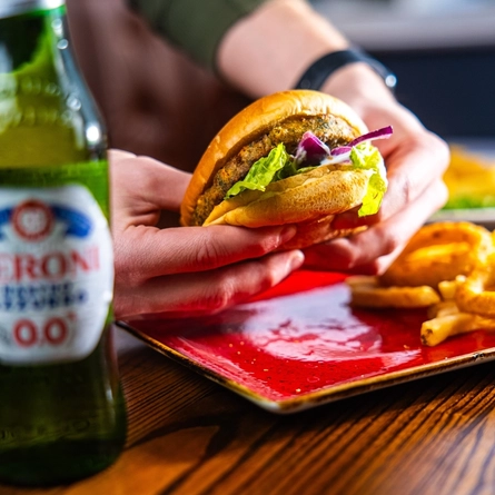 Hands picking a burger up off a plate next to a bottle of Peroni low alcohol beer.