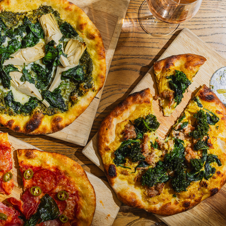 A lifestyle image showing 3 boarded Pizza dishes sat on a table within the interior restaurant seating area at The Four Oaks.